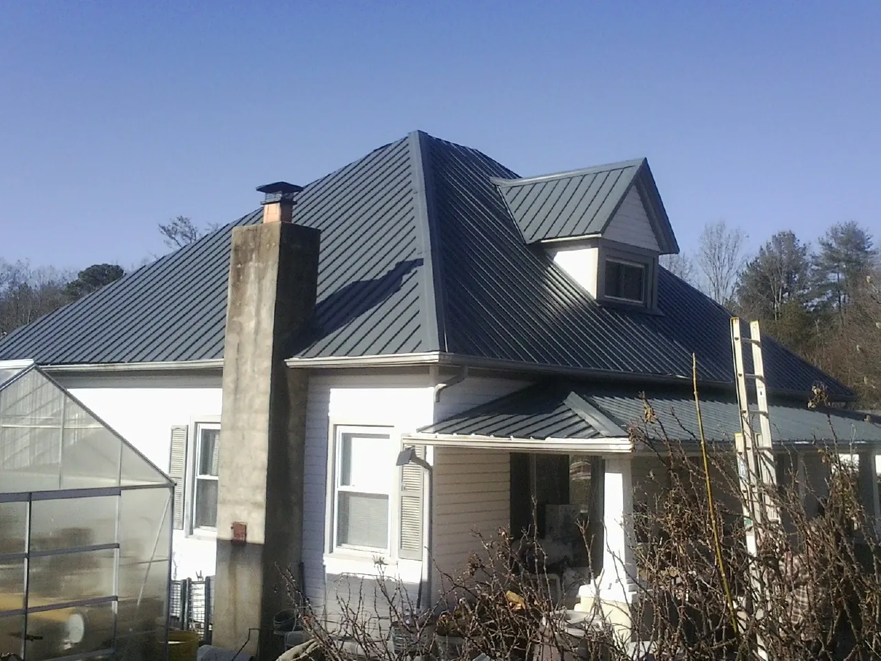 Dark blue standing seam metal roof on a white farmhouse with dormer — Slate & Tile Roof Repair by Roofing Brothers in Pewamo