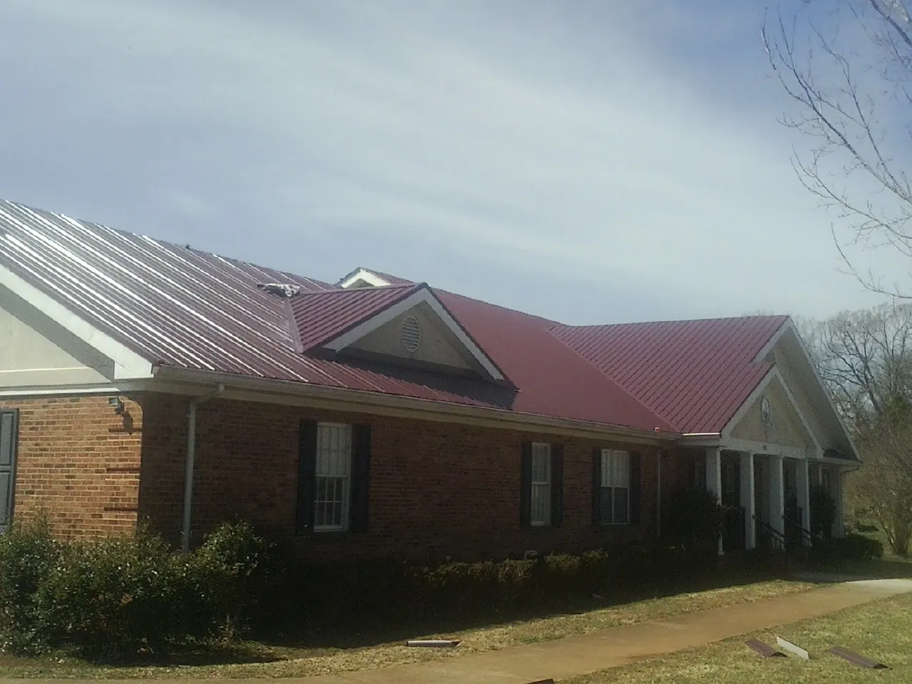Red metal roof with gabled entries on a long brick building, from a Hail Damage Roof Repair job in Pewamo