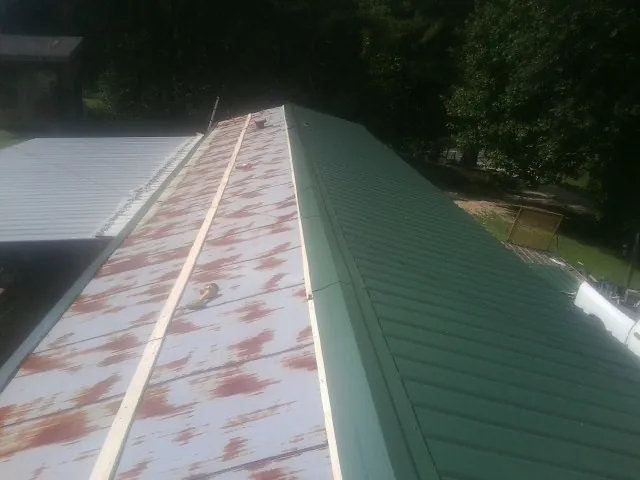 Old rusted panels beside newly installed green metal roofing — Wind Damage Roof Repair by Roofing Brothers in Pewamo