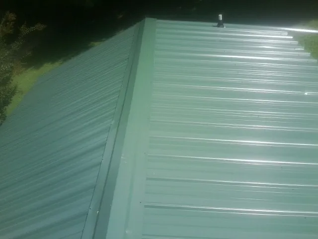New green metal panels meeting at the ridge of a roof — Flat Roof Repair work by our crew in Pewamo