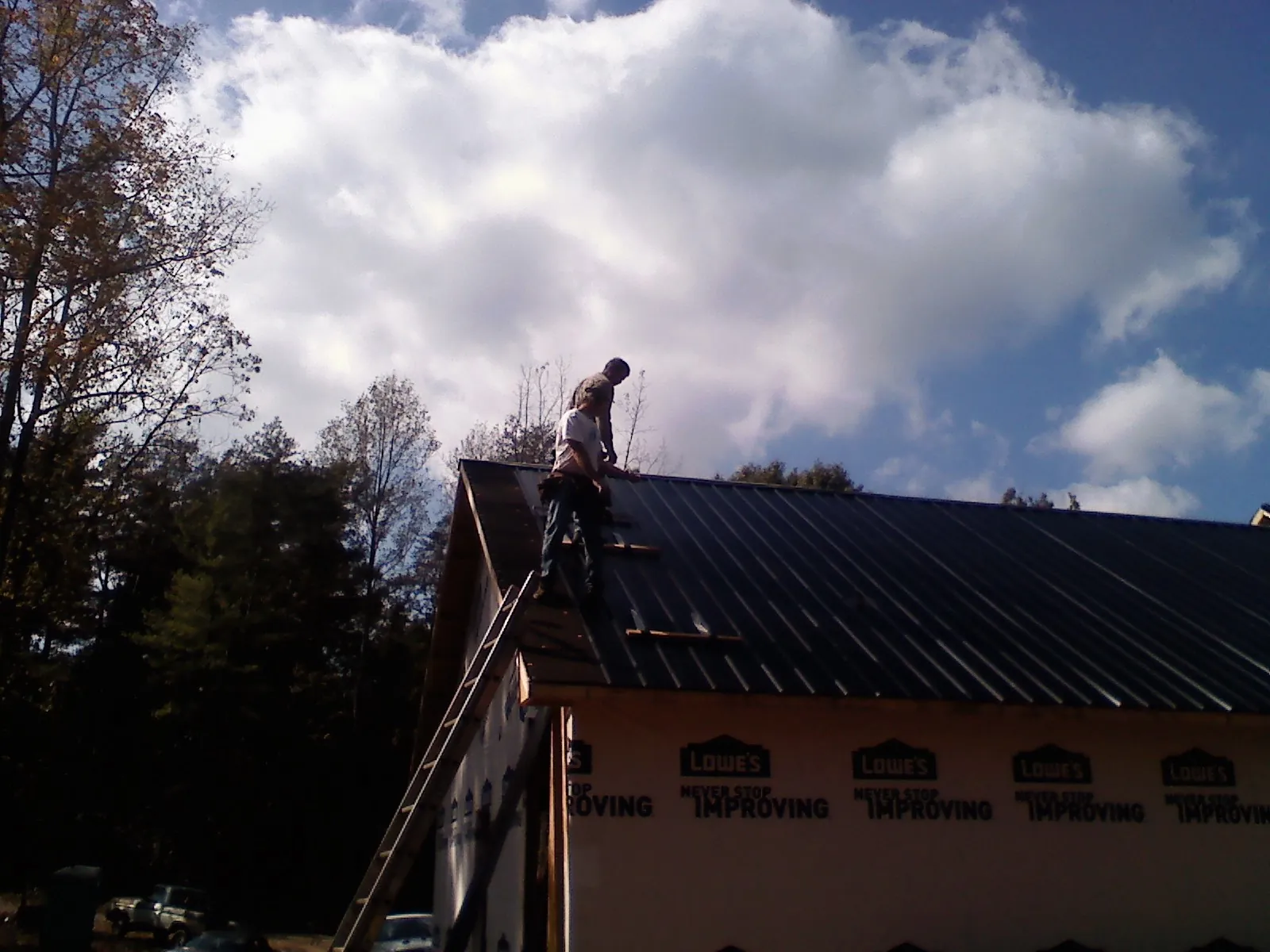 Roofer fastening dark metal panels high against a cloudy sky, from a Roof Inspection job in Pewamo