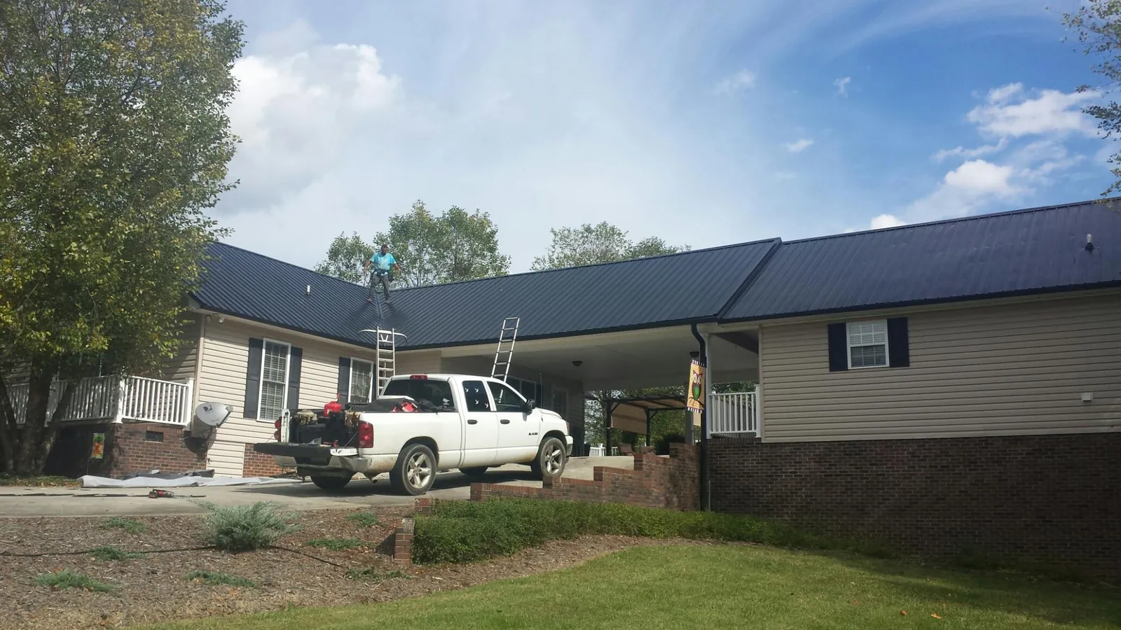 Black metal roof over a home and attached breezeway with ladders set in Pewamo