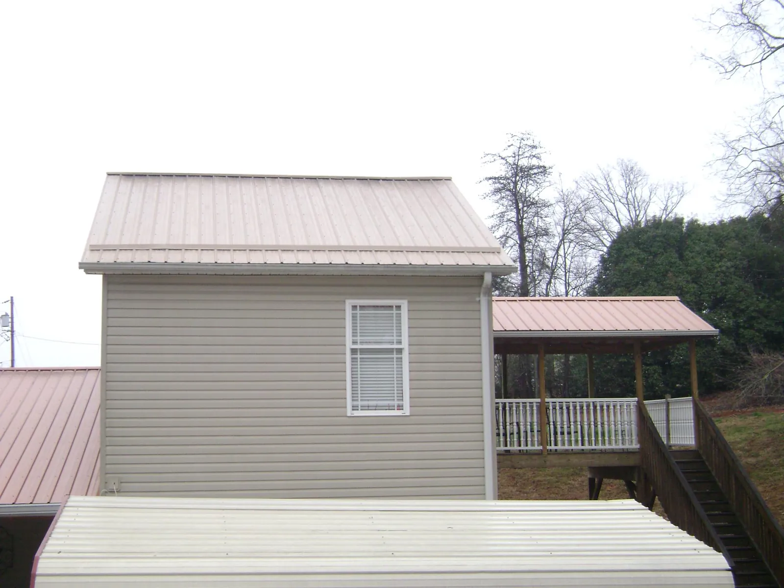 Tan metal roofs on a two story addition and attached porch, from a Roof Replacement job in Pewamo